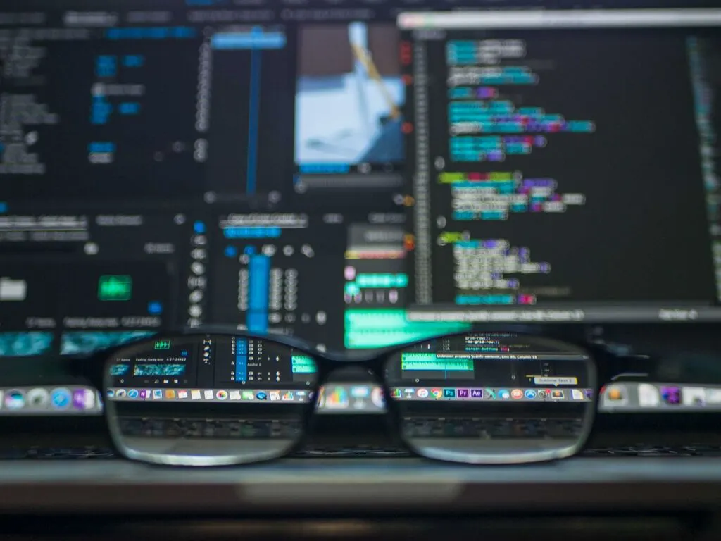 View through glasses to a blurred background of code on screens.